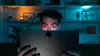 A person is holding a tablet in a dimly lit room with shelves in the background. Náhled obrázku produktu