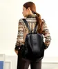 A woman wearing a patterned shirt and dark pants is shown from the back, wearing a black backpack. Náhľad obrázku produktu