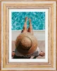 A person wearing a straw hat sits by a pool, with their legs extended towards the water. Produktbild-Vorschau