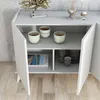 A white console table with its doors open, revealing shelves with cups, a magazine, and stacked plates. Produktbild-Vorschau