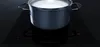 A pot of milk is boiling on a black induction cooktop. Produktbild-Vorschau