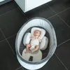 A baby is lying in a baby nest on a tiled floor next to a white cabinet. Produktbild-Vorschau