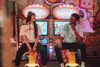 A couple sits on arcade game seats in front of colorful arcade machines. Podgląd zdjęcia produktu