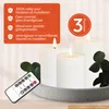 Three white LED candles on a gray concrete tray with some greenery and a remote control in the foreground. Produktbild-Vorschau