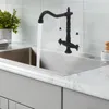 A black faucet with white handles is running water into a stainless steel sink. Podgląd zdjęcia produktu
