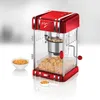 A retro-style red popcorn maker is shown in the center of the image, with unpopped kernels in a bowl to the left and popped popcorn in the machine's bin. There is also a measuring spoon with kernels. Náhled obrázku produktu
