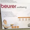 The image shows the packaging of a Beurer Shiatsu Air Compression Seat Cover, with a woman relaxing on it. Voir les images du produit