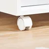 A close-up of a white caster wheel attached to a white furniture item, resting on a light brown wooden floor. Podgląd zdjęcia produktu