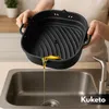 A person is holding a black silicone air fryer liner over a sink, draining oil from it. Náhled obrázku produktu