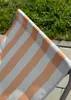 A close-up view of a striped beach chair fabric with grass and paving stones in the background. Produktbild-Vorschau