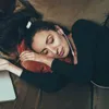 A woman is sleeping on a couch with earbuds in her ears and a laptop nearby. Produktbild-Vorschau