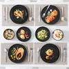A collage of six different table settings, each featuring a black plate with food and cutlery. Produktbild-Vorschau