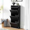 A black shoe cabinet with four flip-down compartments is shown in a room with a window and a basket of blankets. Voir les images du produit
