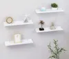 Four white wall shelves are mounted on a light gray wall, each displaying decorative items. Produktbild-Vorschau