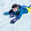 A young boy is lying on the snow, wearing winter clothes and gloves. Produktbild-Vorschau