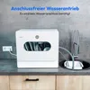 A white compact dishwasher is shown on a kitchen countertop next to a sink with a faucet. The dishwasher is connected to a power outlet. Produktbild-Vorschau