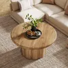 A round wooden coffee table with a fluted base is placed on a textured rug in front of a sectional sofa. Produktbild-Vorschau