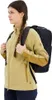A young woman wearing a beige and brown jacket is shown from the side, wearing a black backpack. Anteprima dell’immagine prodotto