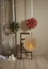 Three paper star lanterns are hanging, one on a door and two on a chair, with candles in the foreground. Podgląd zdjęcia produktu