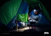 A person is cooking inside a tent at night, illuminated by a headlamp. Produktbild-Vorschau