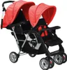 A tandem stroller with red canopies and black seats, shown from a front-side angle against a white background. Náhled obrázku produktu
