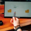 A hand holding a Verbatim flash drive in front of a computer screen displaying a file transfer process. Náhľad obrázku produktu