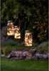 Three mason jar lanterns with fairy lights hanging from a tree branch in a garden at dusk. Produktbild-Vorschau
