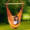 A woman relaxing in a colorful hammock chair hanging from a tree in a grassy yard. Produktbild-Vorschau