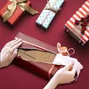 Hands are shown unwrapping a gift box, revealing a cardboard insert with outlines of bottles. Produktbild-Vorschau