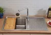 A stainless steel kitchen sink with a cutting board, faucet, and dish drying rack. Produktbild-Vorschau