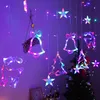 Christmas lights in the shape of bells, reindeer, and trees, hanging in front of a Christmas tree and a wall. Produktbild-Vorschau