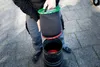 A person is holding a black cylindrical filter with a green top and red rim over a black cylindrical container. Produktbild-Vorschau