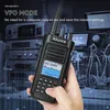 A hand holding a black walkie-talkie with a screen displaying information, with electronic equipment in the background. Produktbild-Vorschau