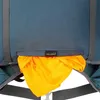 A close-up view of the bottom section of a backpack, showing a stored orange rain cover. Produktbild-Vorschau