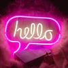 A pink neon sign shaped like a speech bubble with the word "hello" in white neon, placed on a fluffy pink background, with a book and a perfume bottle in the foreground. Anteprima dell’immagine prodotto
