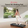 A woman is walking on a YESOUL W2 Walking Pad in a modern room, with a large screen displaying a virtual golf course and workout statistics. Produktbild-Vorschau