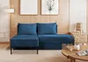 A blue sectional sofa in a living room setting with artwork on the wall and a wooden side table. Produktbild-Vorschau