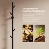 A black towel warmer with a tree-like design is shown on a light beige wall, with two smaller inset images of a bird on a branch and a seedling being held by hands. Produktbild-Vorschau