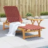 A red woven chaise lounge chair with a white towel draped over it, placed on a tiled patio next to a small wooden side table with a hat and a glass on it. A wooden fence is in the background. Podgląd zdjęcia produktu