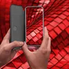 Hands holding a smartphone with a flip case, against a red tiled background. Produktbild-Vorschau
