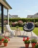 A cozy outdoor seating area with two chairs, a small table, and potted plants on a wooden deck, with a garden and houses in the background. Produktbild-Vorschau