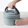 Hands holding a round, multi-tiered food container with a handle. Náhled obrázku produktu