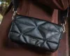 A person wearing a brown coat is holding a black quilted handbag. Produktbild-Vorschau