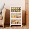 A white storage cabinet with clear doors filled with various food items and boxes, placed next to a beige sofa in a room with light pink walls and wooden flooring. Anteprima dell’immagine prodotto