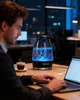 A man is working on a laptop at a desk in an office at night, with a glass kettle boiling water with blue LED lights. Produktbild-Vorschau