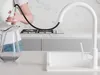 A person is using a white kitchen faucet with a pull-out spray to fill a glass pitcher. Produktbild-Vorschau