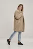 A woman is posing in a studio setting wearing a fluffy beige coat and light blue jeans. Produktbild-Vorschau