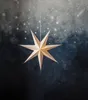A white, seven-pointed paper star hangs in front of a dark, starry background. Podgląd zdjęcia produktu