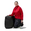 Frau in roter Jacke und schwarzen Hosen kniet neben einem kompakten; schwarzen Beutel mit dem Logo von Berghaus. Anteprima dell’immagine prodotto