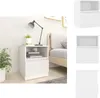 A white nightstand with a drawer and an open shelf, placed next to a bed in a bedroom setting. A lamp and books are on the shelf, and a plant is to the left. Voir les images du produit